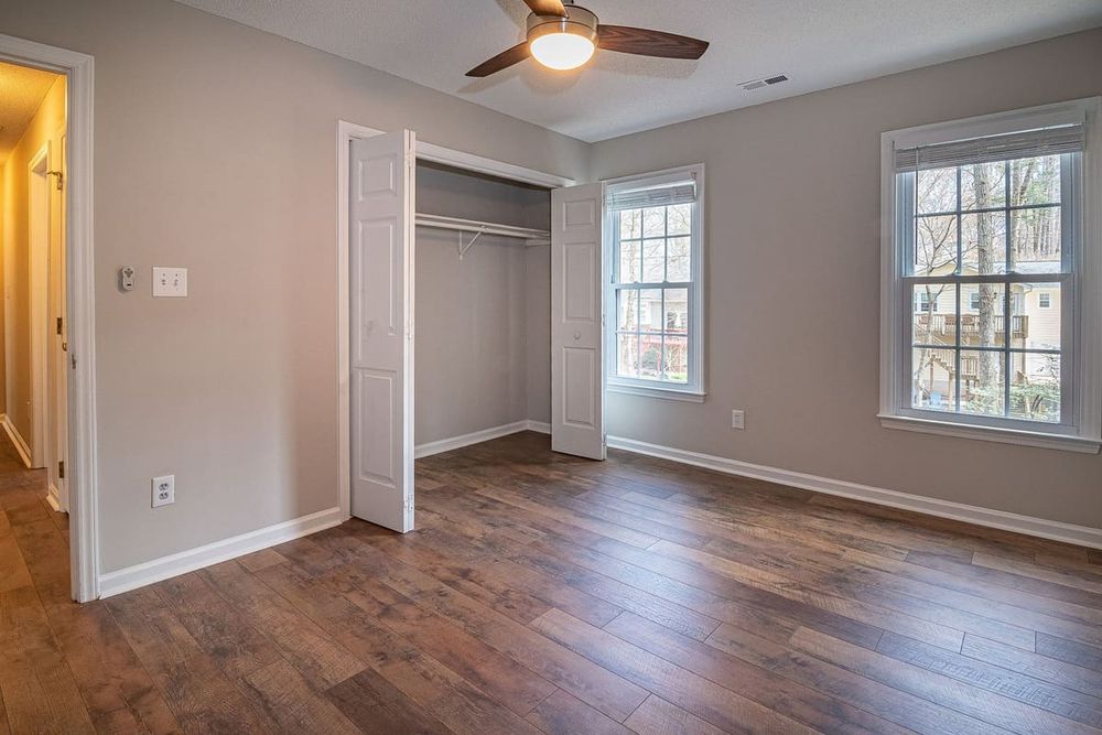Spacious empty bedroom with wooden floor, ceiling fan, and open closet in a modern home.