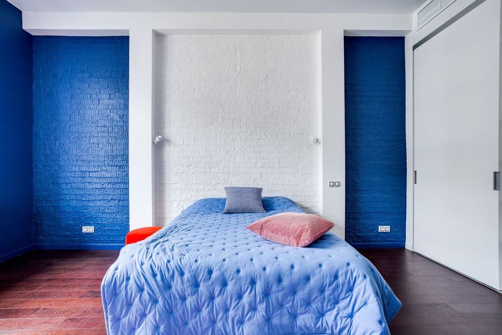 Modern bedroom with navy blue walls, cozy bed, and stylish pillows.