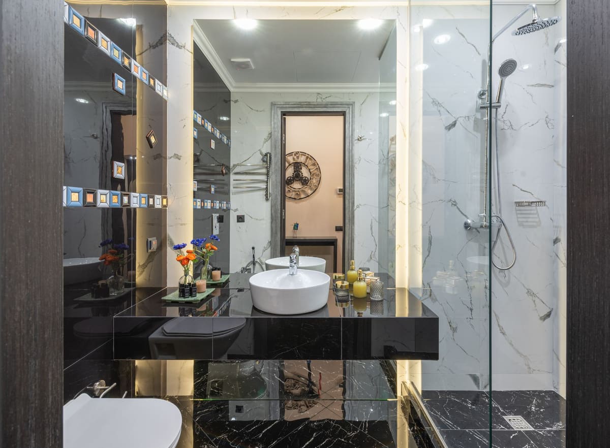 Interior of contemporary bathroom with bidet and black cupboard with sink and decorations placed near glass transparent shower cabin at home