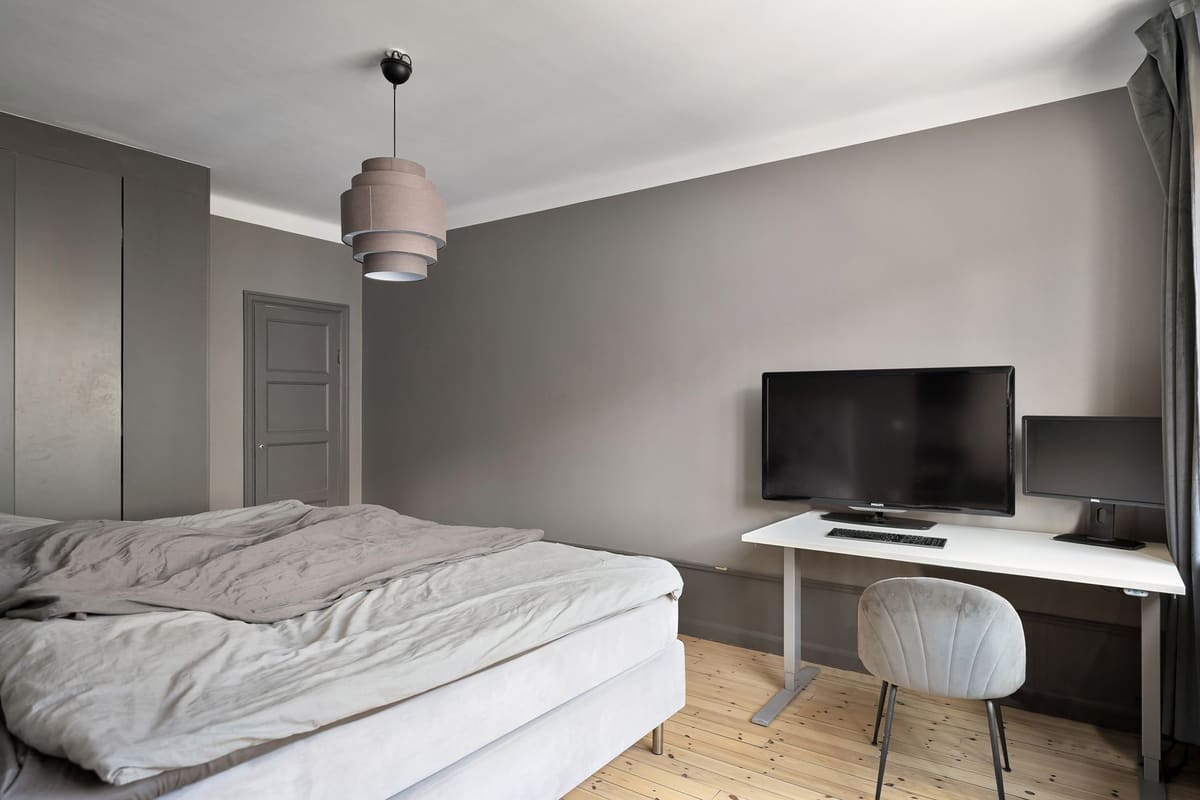 Sleek modern bedroom with a minimalist design featuring a computer workstation and gray walls.