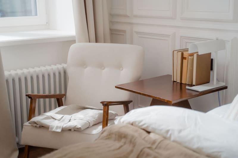 A serene bedroom corner featuring an armchair, folded bathrobe, and a side table with books.