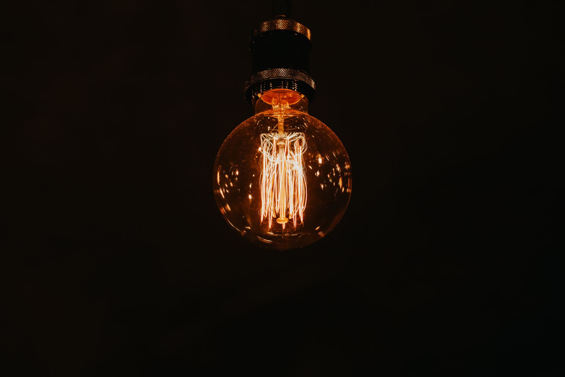From below of glowing stylish lamp with warm light hanging in dark room