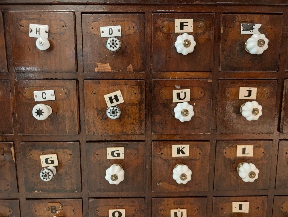 Antique wooden drawer cabinet with unique labeled knobs in a vintage style.