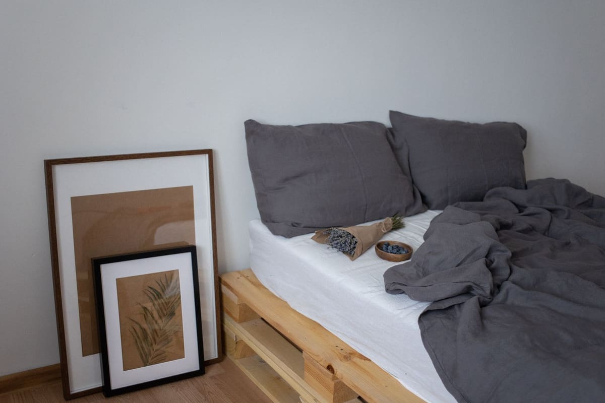 Stylish minimalist bedroom featuring grey bedding and framed art on wooden pallet bed.