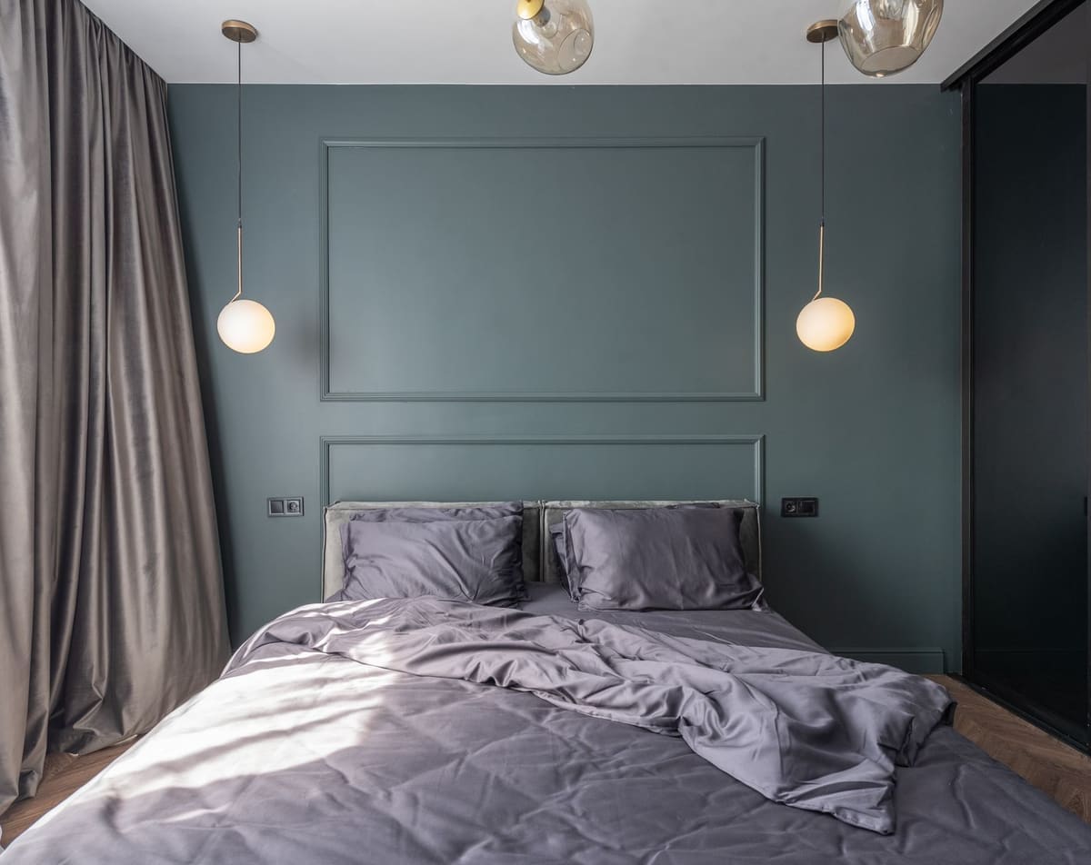 Interior design of modern bedroom with unmade bed under luminous lamps at sunlight