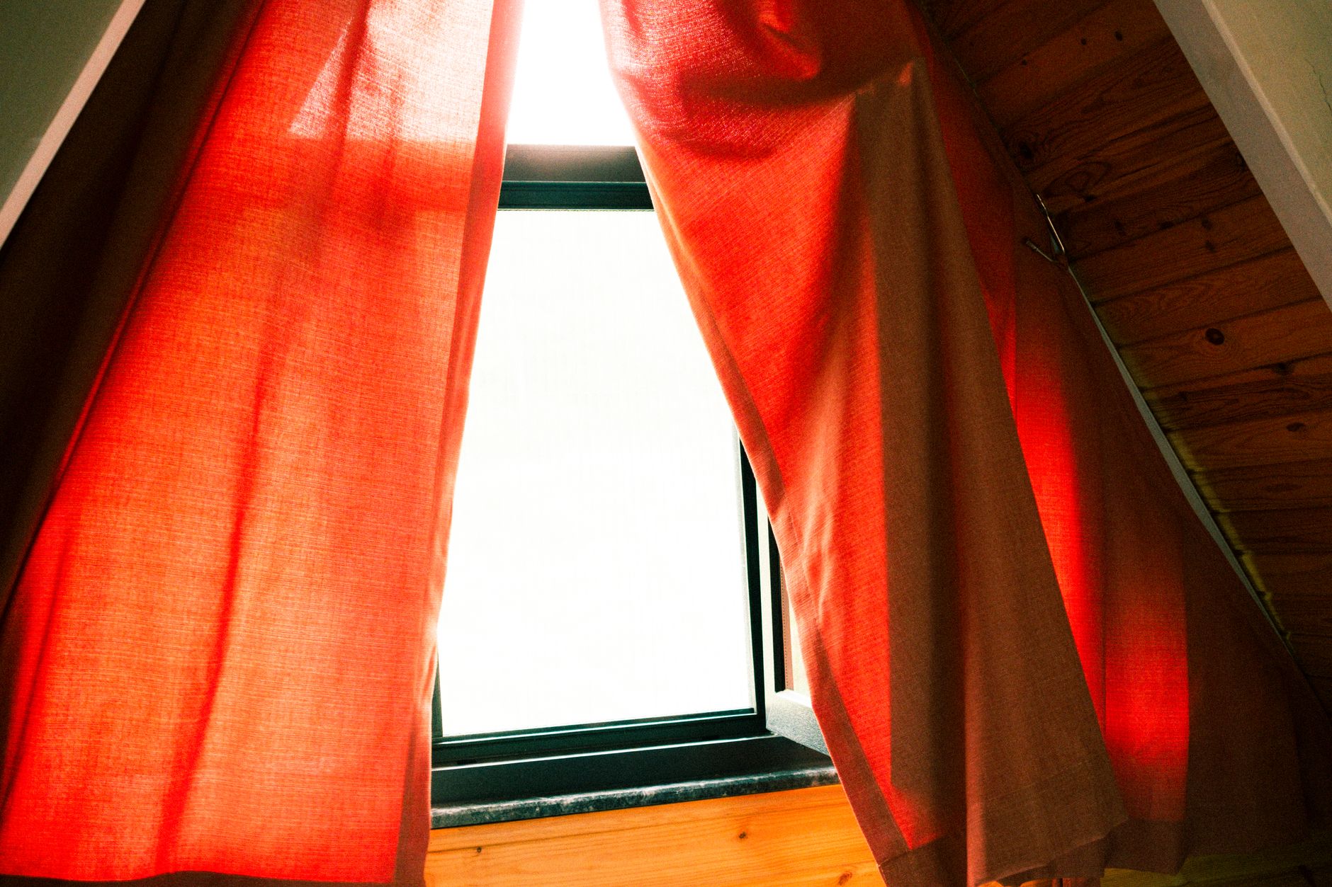 A cozy attic window with red curtains letting in warm sunlight, creating a serene indoor atmosphere.