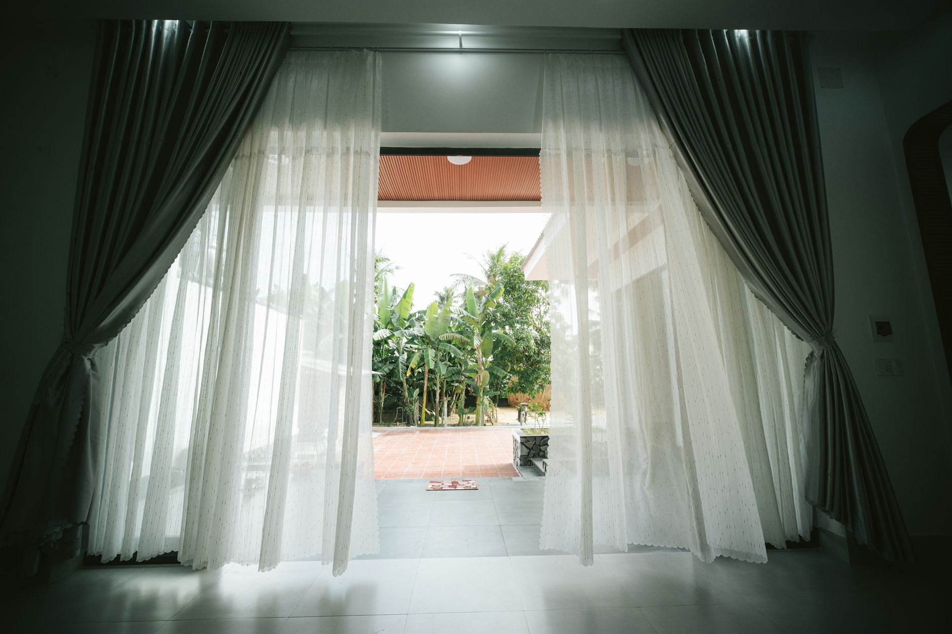 View of open terrace through white curtains, revealing a lush garden.