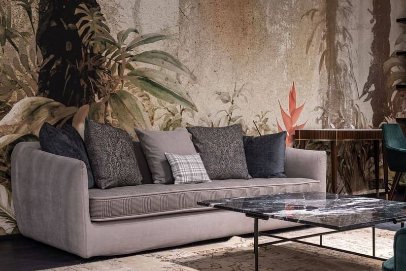 Comfortable sofa with pillows placed at wall with painted leaves in modern spacious room with table on rug at home