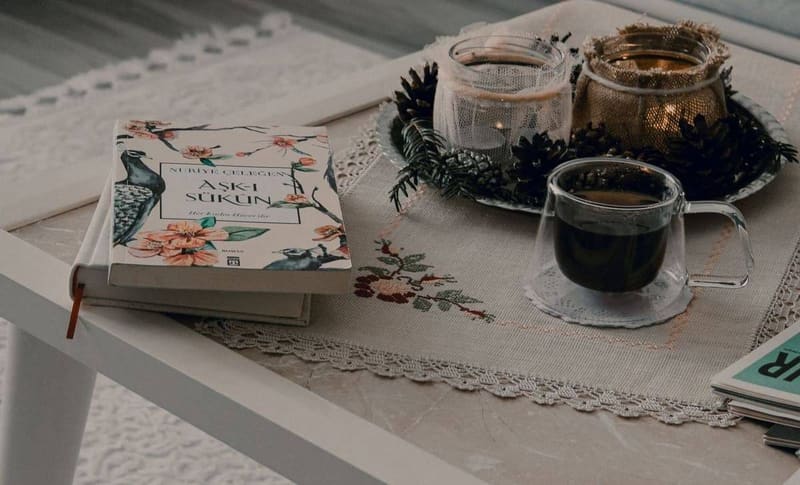 Warm and cozy coffee table setting with book, candles, and hot drink, perfect for a relaxing morning routine.