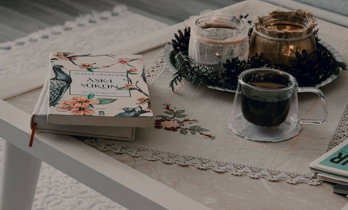 Warm and cozy coffee table setting with book, candles, and hot drink, perfect for a relaxing morning routine.