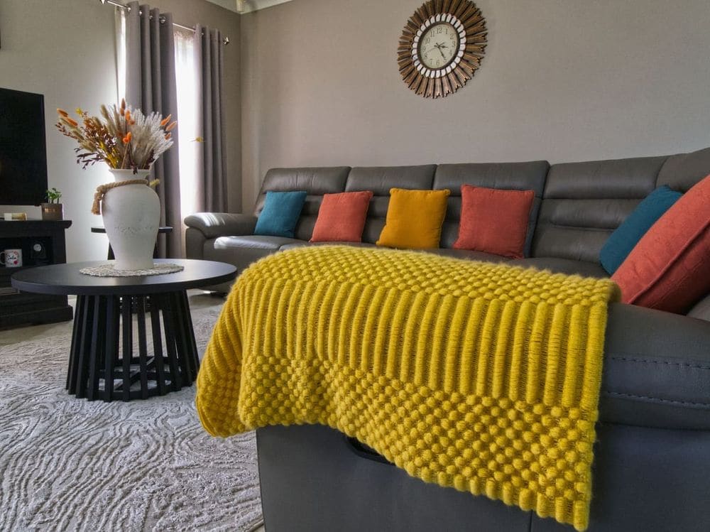 A stylish living room with colorful cushions and a yellow throw. Cozy modern design.