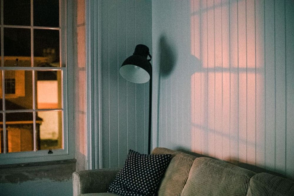 A warm and inviting living room featuring a soft couch and floor lamp casting shadows on the wall.