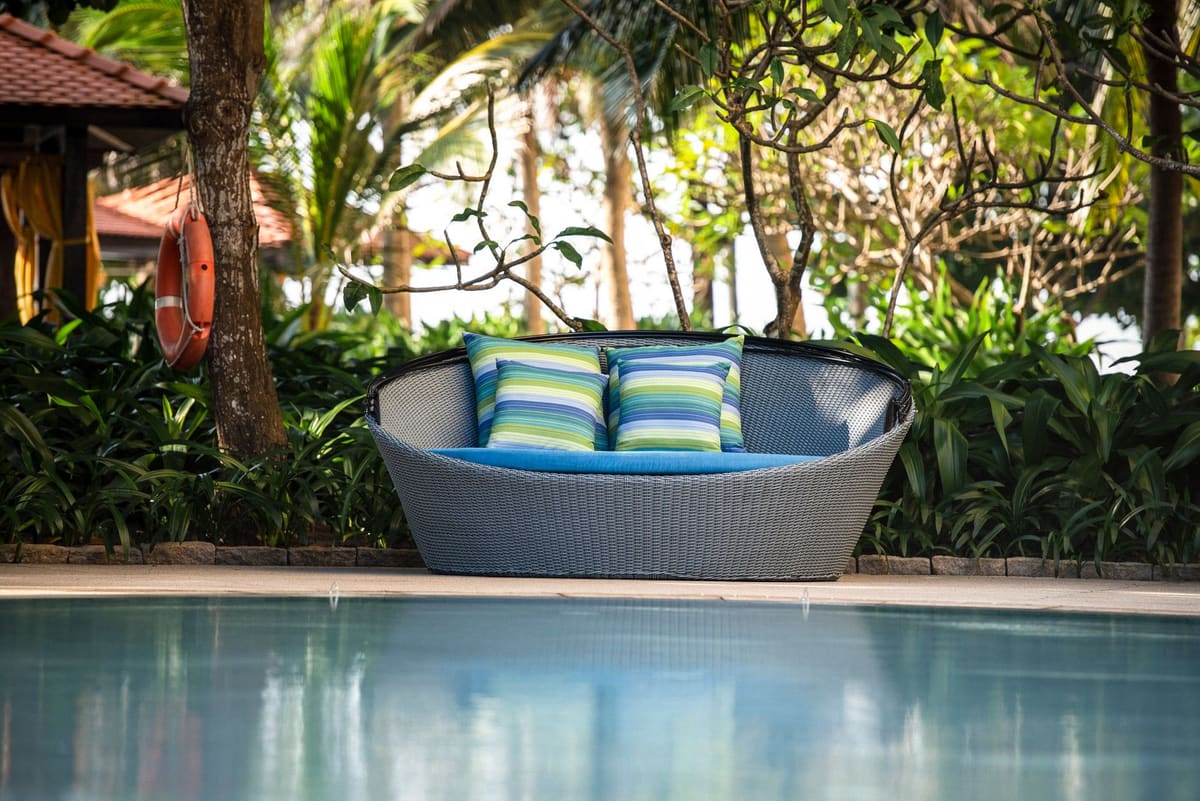 Inviting outdoor wicker chair with pillows, surrounded by lush plants by the poolside.