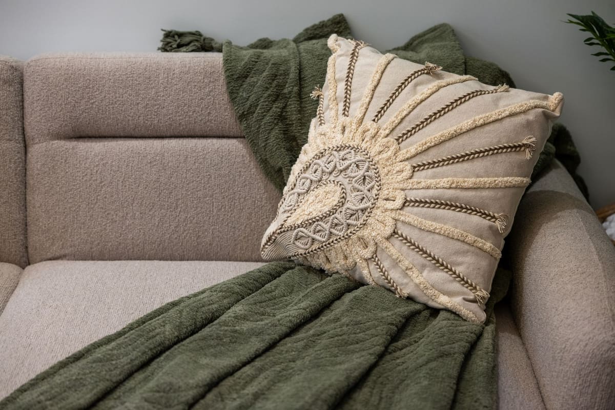 Comfortable beige couch with decorative boho pillow and green throw, perfect for a cozy interior setting.