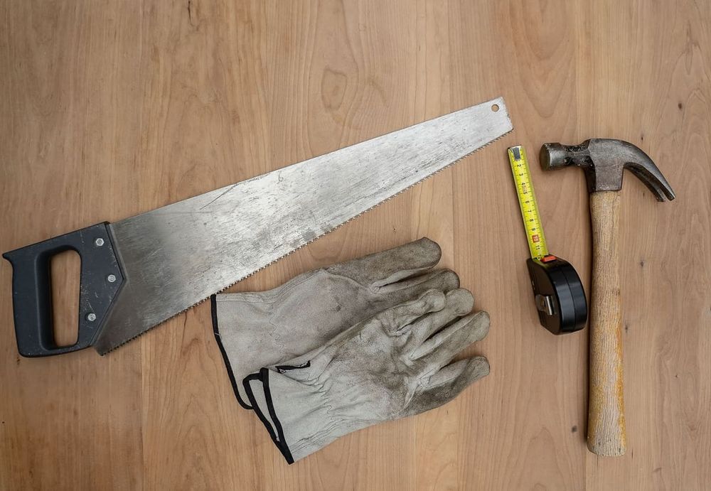Flat lay of essential carpentry tools including a saw, hammer, and tape measure on wooden surface.