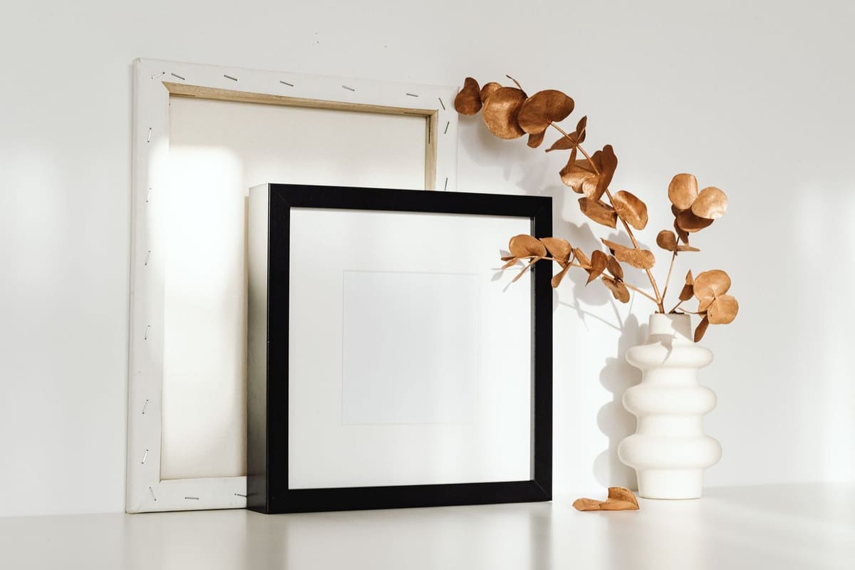 A minimalist home setting with empty frames and a vase with dried eucalyptus branches on a white surface.
