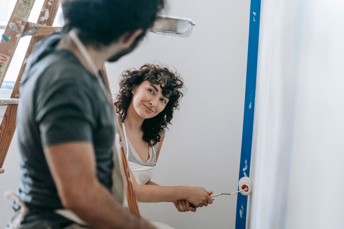 A happy couple painting walls together in their home, enjoying a playful moment during renovation.