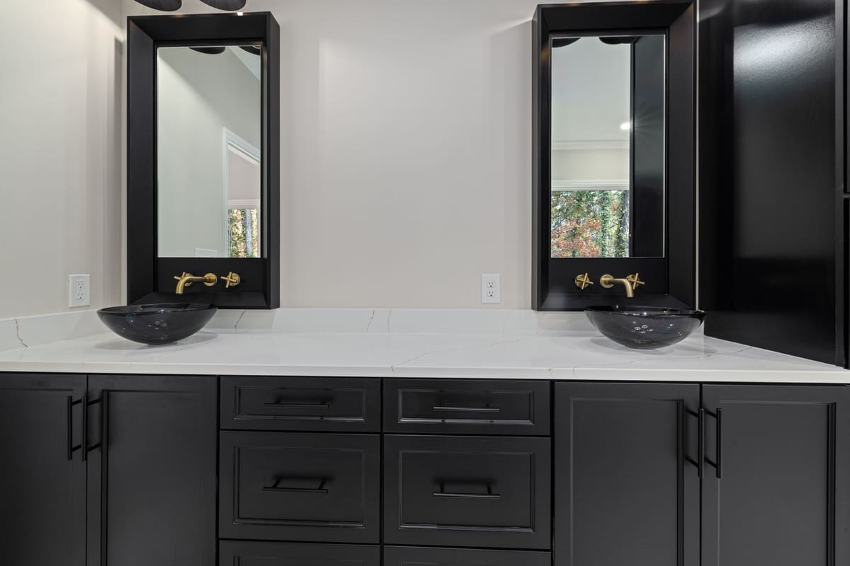 Elegant bathroom featuring black cabinets, vessel sinks, and gold hardware.