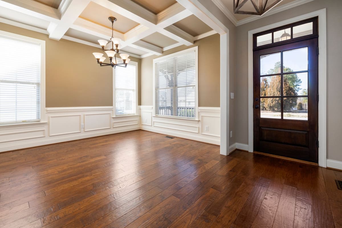 Spacious empty living room with wooden flooring, large windows, and ceiling lights.