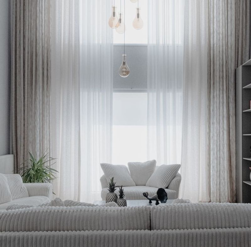 A minimalist living room with soft white sofas and large curtains, creating a cozy atmosphere.