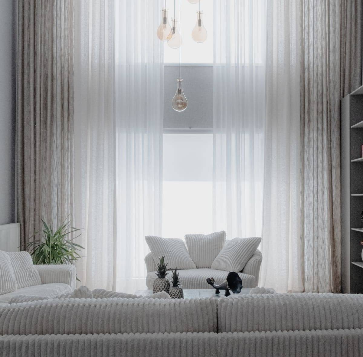 A minimalist living room with soft white sofas and large curtains, creating a cozy atmosphere.