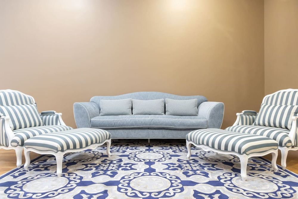 Luxurious living room interior featuring a vintage blue sofa and striped chairs on a patterned carpet.