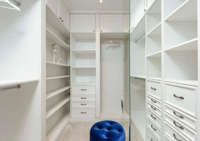 Soft blue velour pouf in white built in closet with empty shelves and racks in classic styled apartment