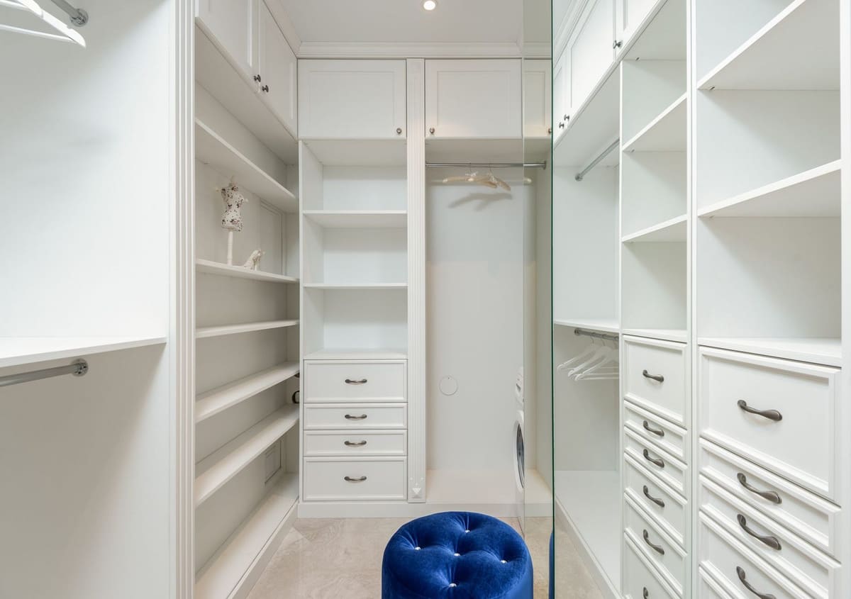 Soft blue velour pouf in white built in closet with empty shelves and racks in classic styled apartment