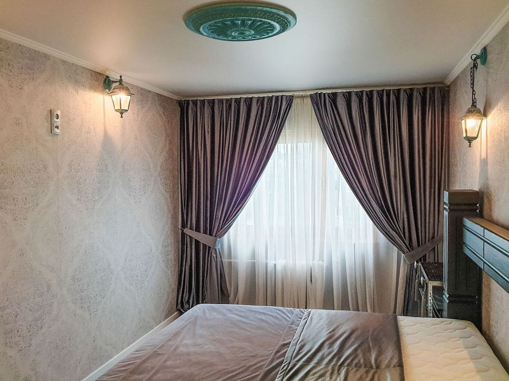 A serene bedroom featuring elegant curtains and classic wall sconces.