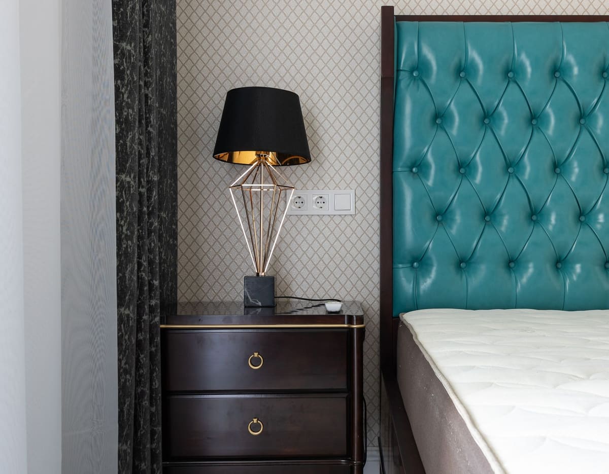 Modern bedroom interior with lamp between mattress on bed with upholstery and curtains at home