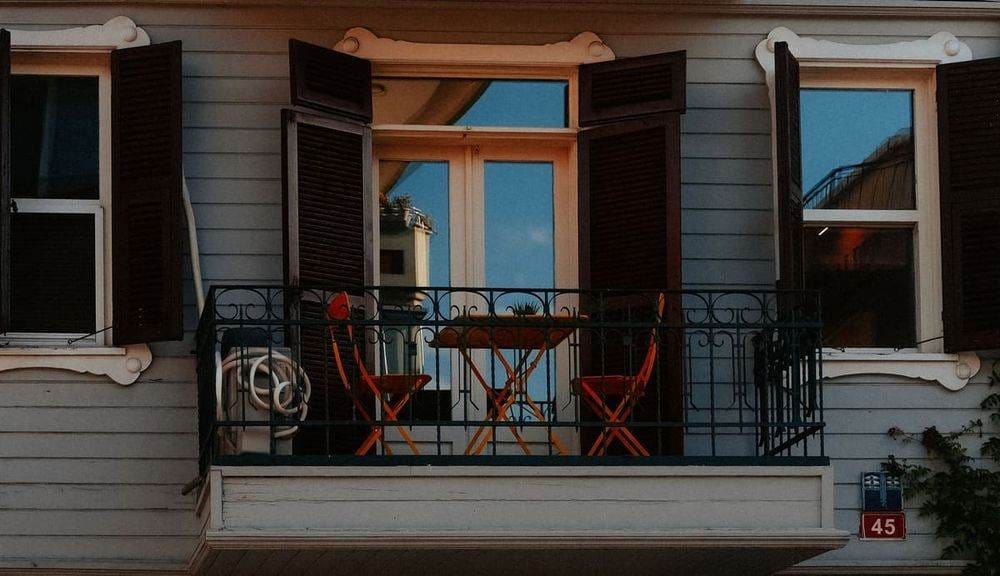 Charming balcony with orange chairs, table, and open windows on a sunny day.