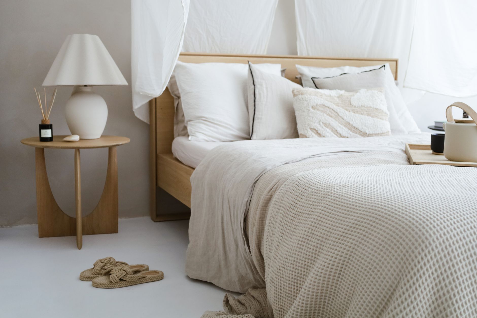 A minimalist bedroom with neutral tones featuring cozy bedding, a side table, and soft lighting.