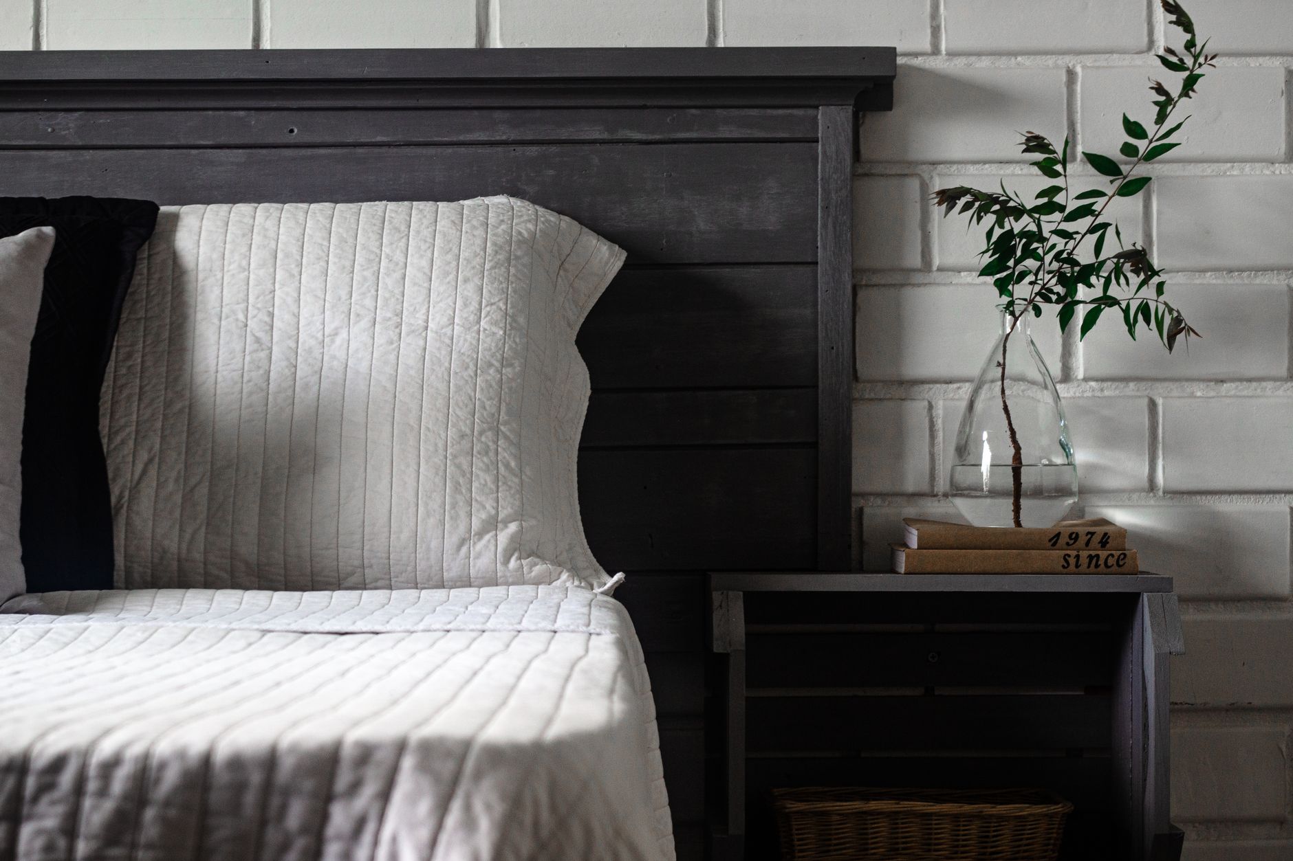 Chic rustic bedroom with cozy bedding, modern nightstand and glass vase.