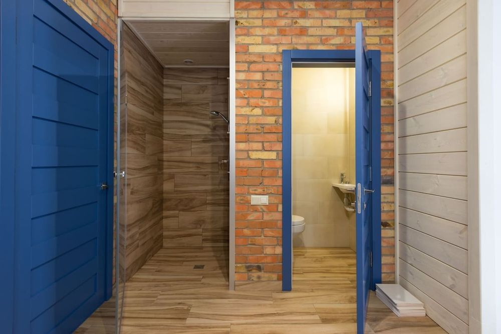 Contemporary bathroom interior with wooden and brick materials, featuring blue doors and a shower area.