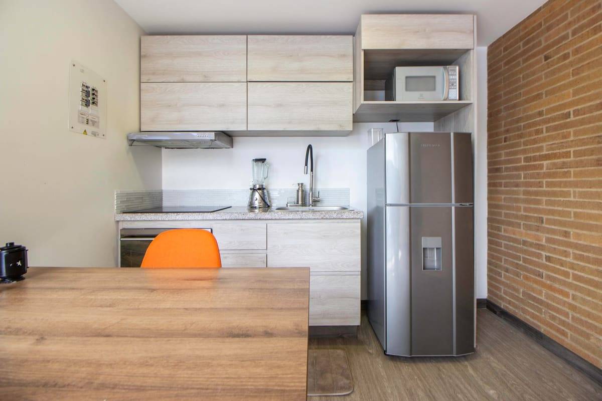 A modern kitchen featuring wooden cabinets, stainless appliances, and an orange chair.