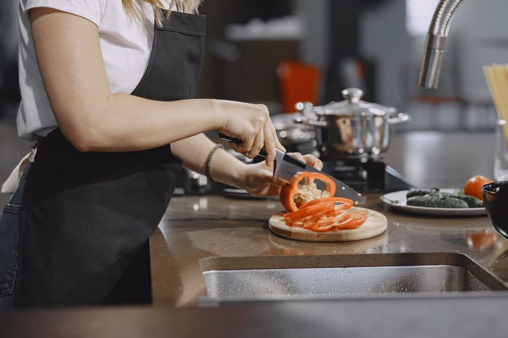 Woman slicing tomatoes in a modern kitchen setting with cooking equipment on the counter.