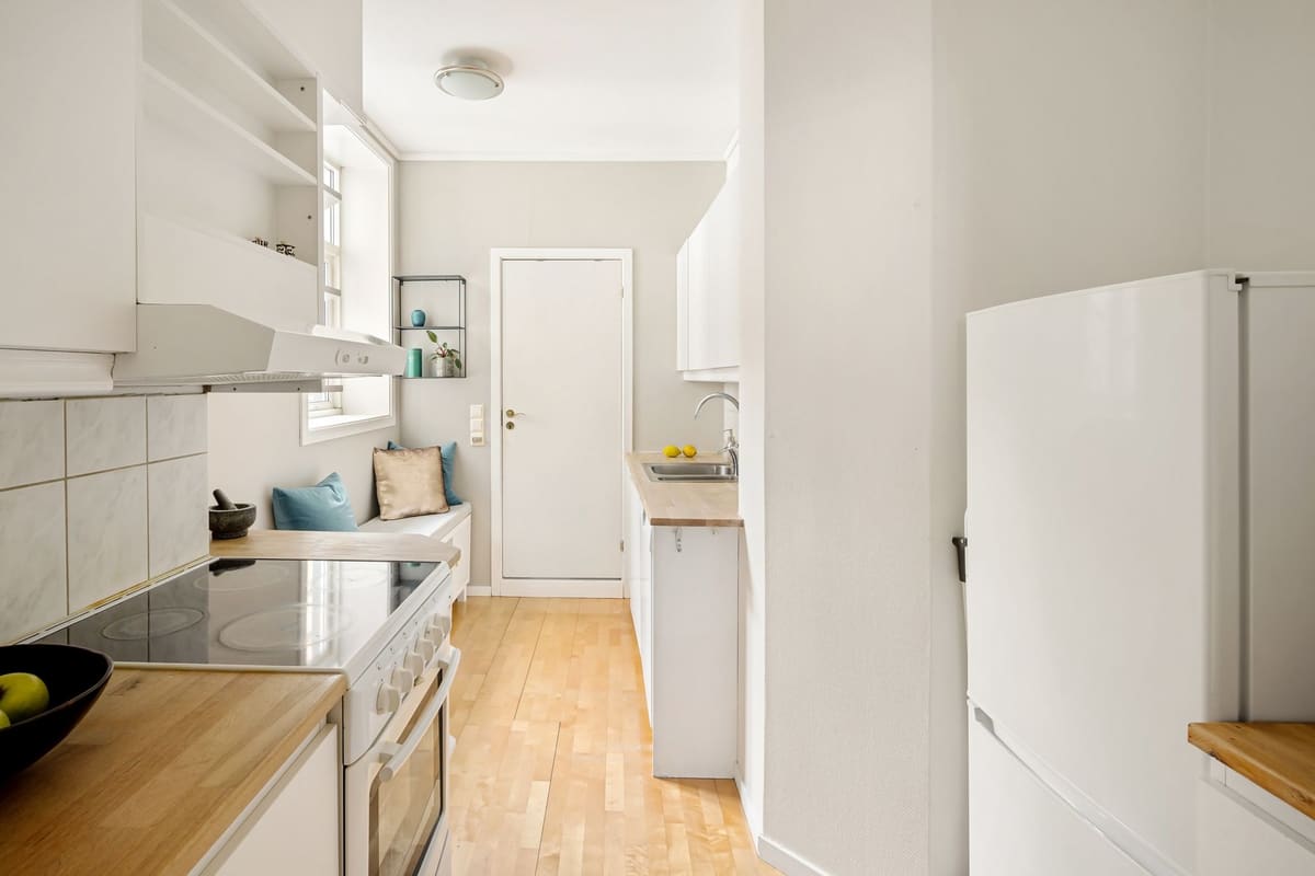 Modern white kitchen with wooden floors and minimalistic design, featuring a cozy seating area.