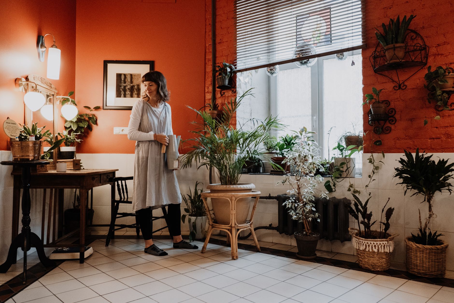 Woman arranging indoor plants in a stylish, warm-toned room.