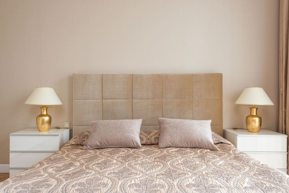 Interior of bedroom with big bed with soft headboard and lamps placed on nightstands in daylight