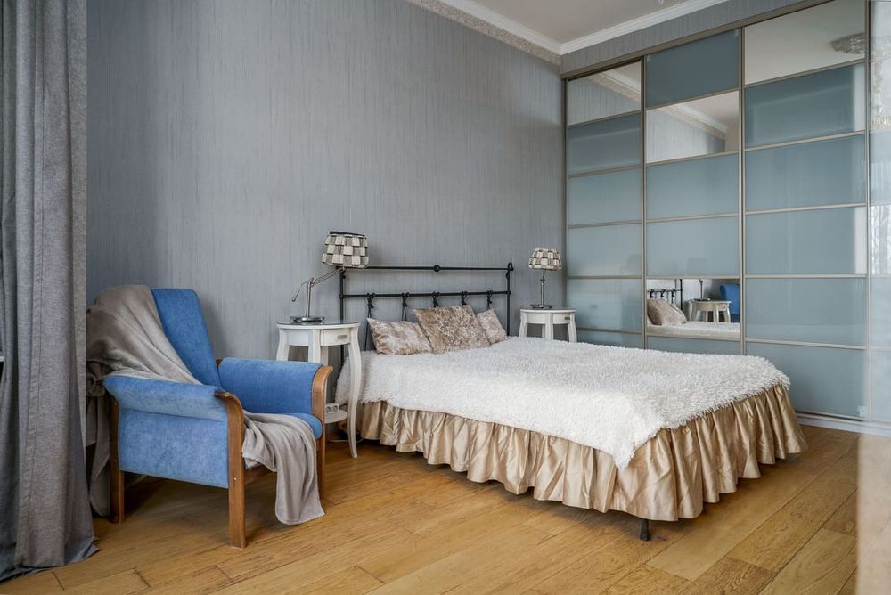 Styled bedroom with armchair, bed, nightstands, and wardrobe in modern design.